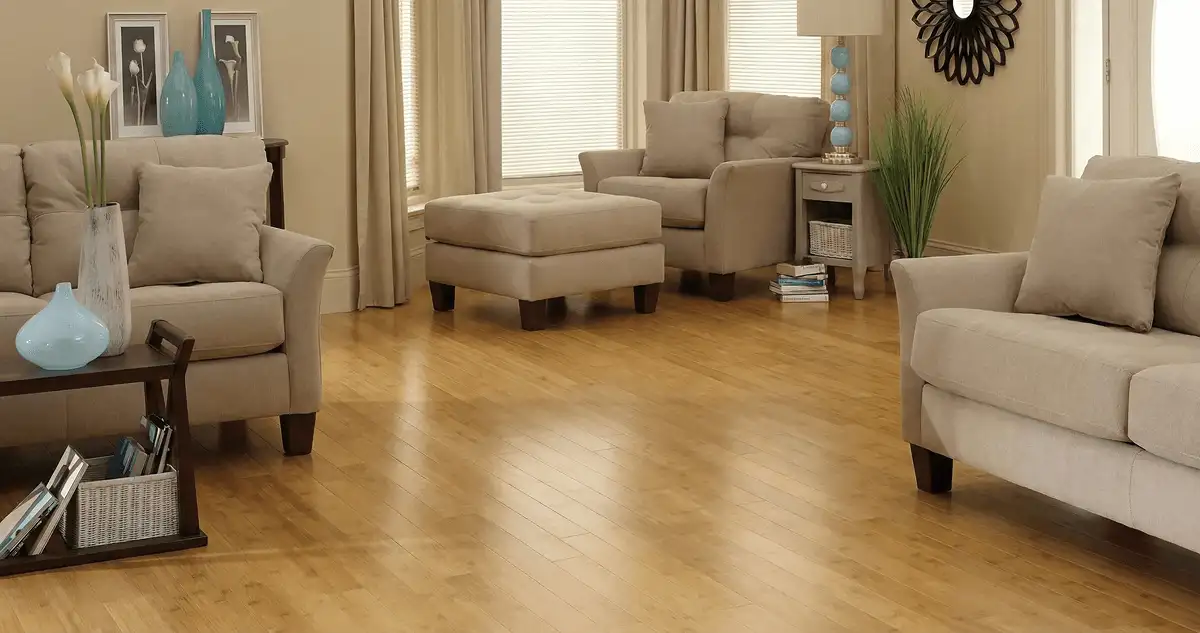 A living room with professionally installed bamboo flooring, beige sofas, a matching ottoman, a side table with a blue lamp, vases, framed pictures, and large windows with blinds and curtains in Seattle, WA