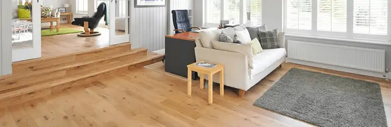 A modern living room with professionally installed laminate flooring, a beige sofa, a small side table, a gray rug, and large windows with white shutters in Seattle, WA